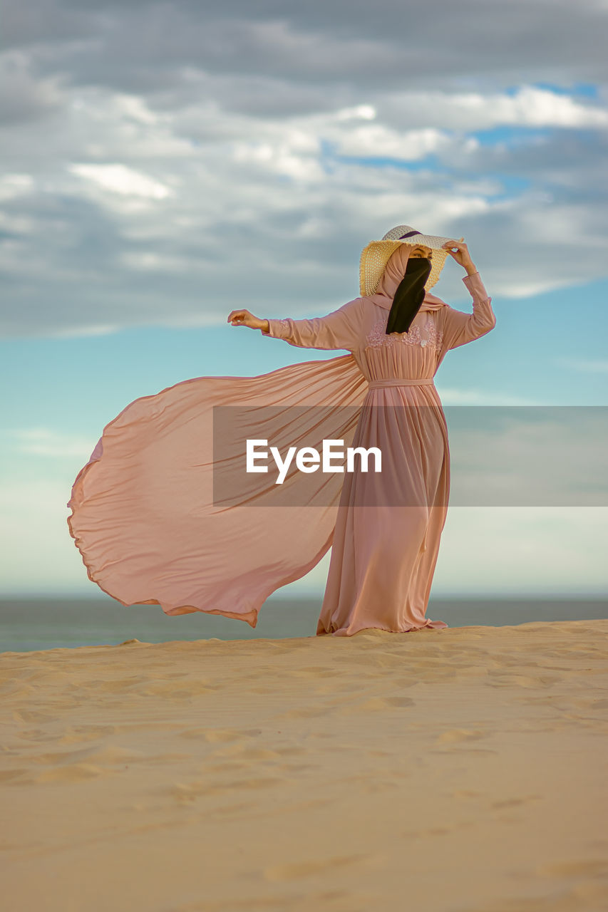 Muslim girl with pink dress waving her dress and walking on the sand dunes.