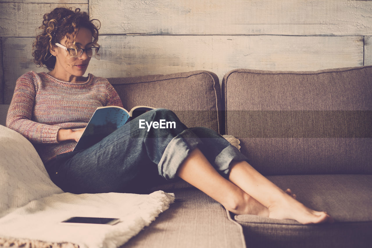 YOUNG WOMAN SITTING ON SOFA IN BOOK