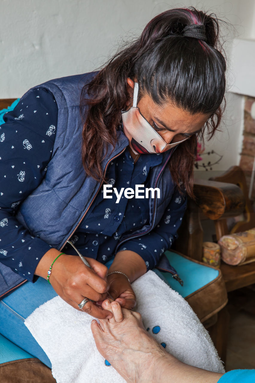 Woman wearing mask doing pedicure to patient