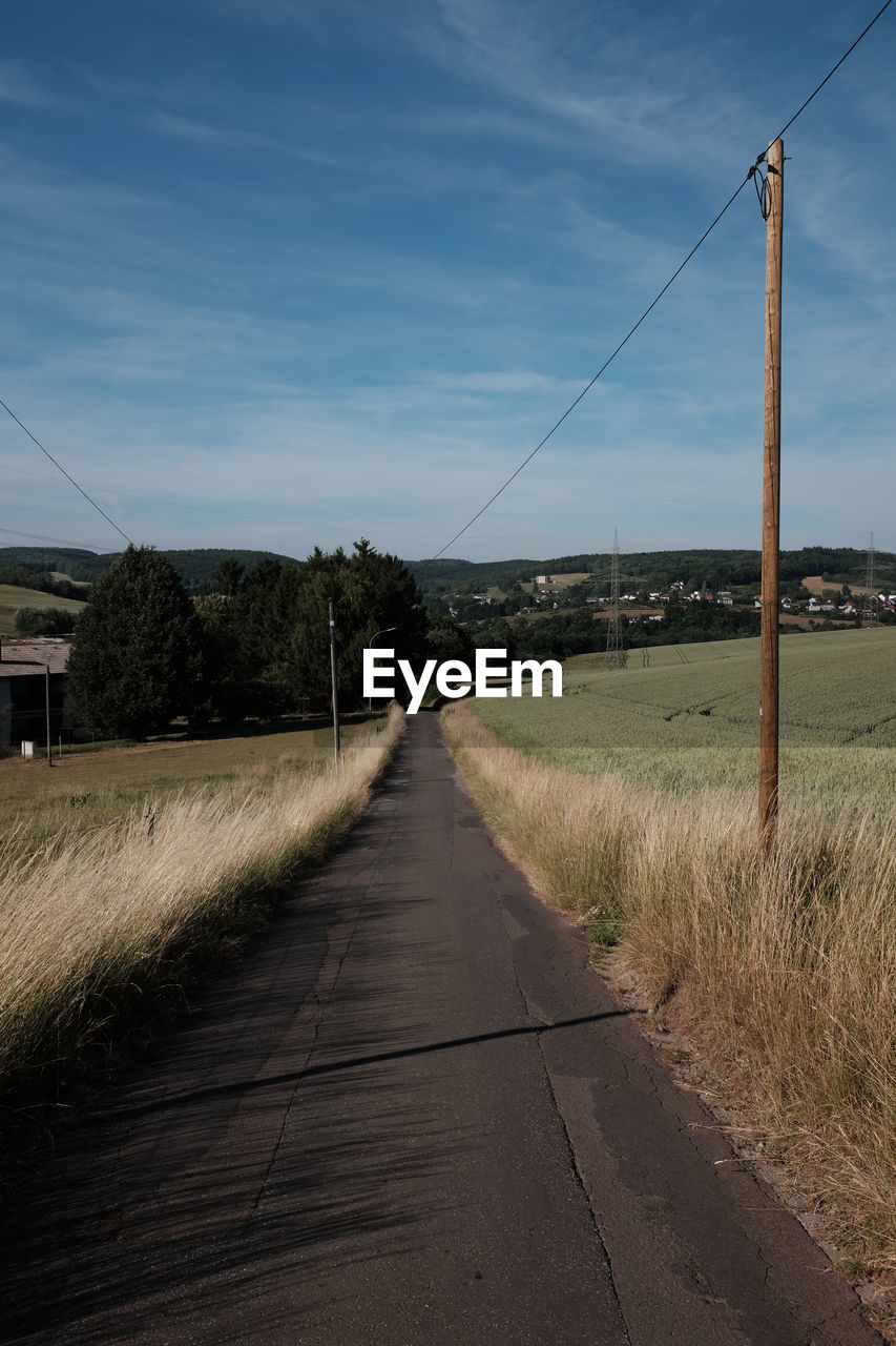 VIEW OF ROAD BY FIELD AGAINST SKY