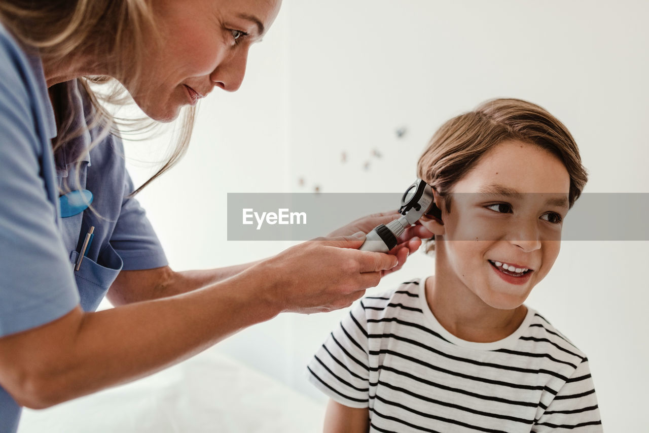 Doctor examining boy's ear with otoscope in medical examination room