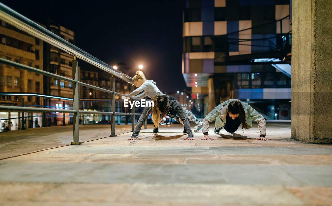 Female sport team doing push ups during training on the city at night