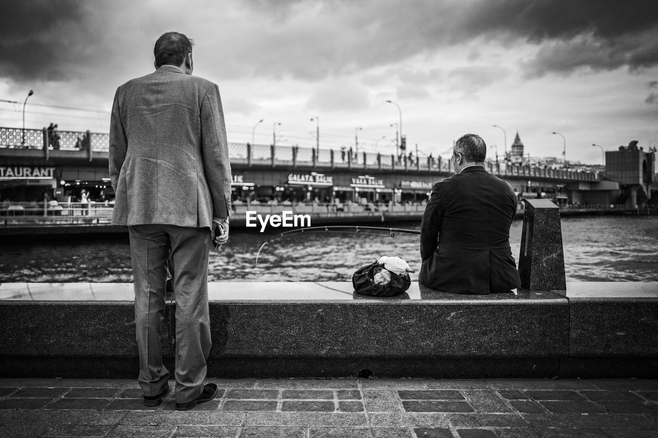 Rear view of men by river in city against sky