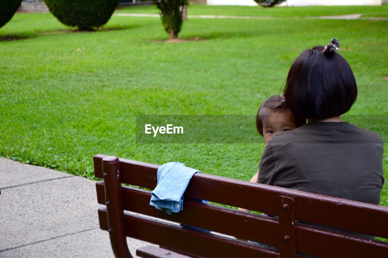 Rear view of mother and daughter sitting on bench in park