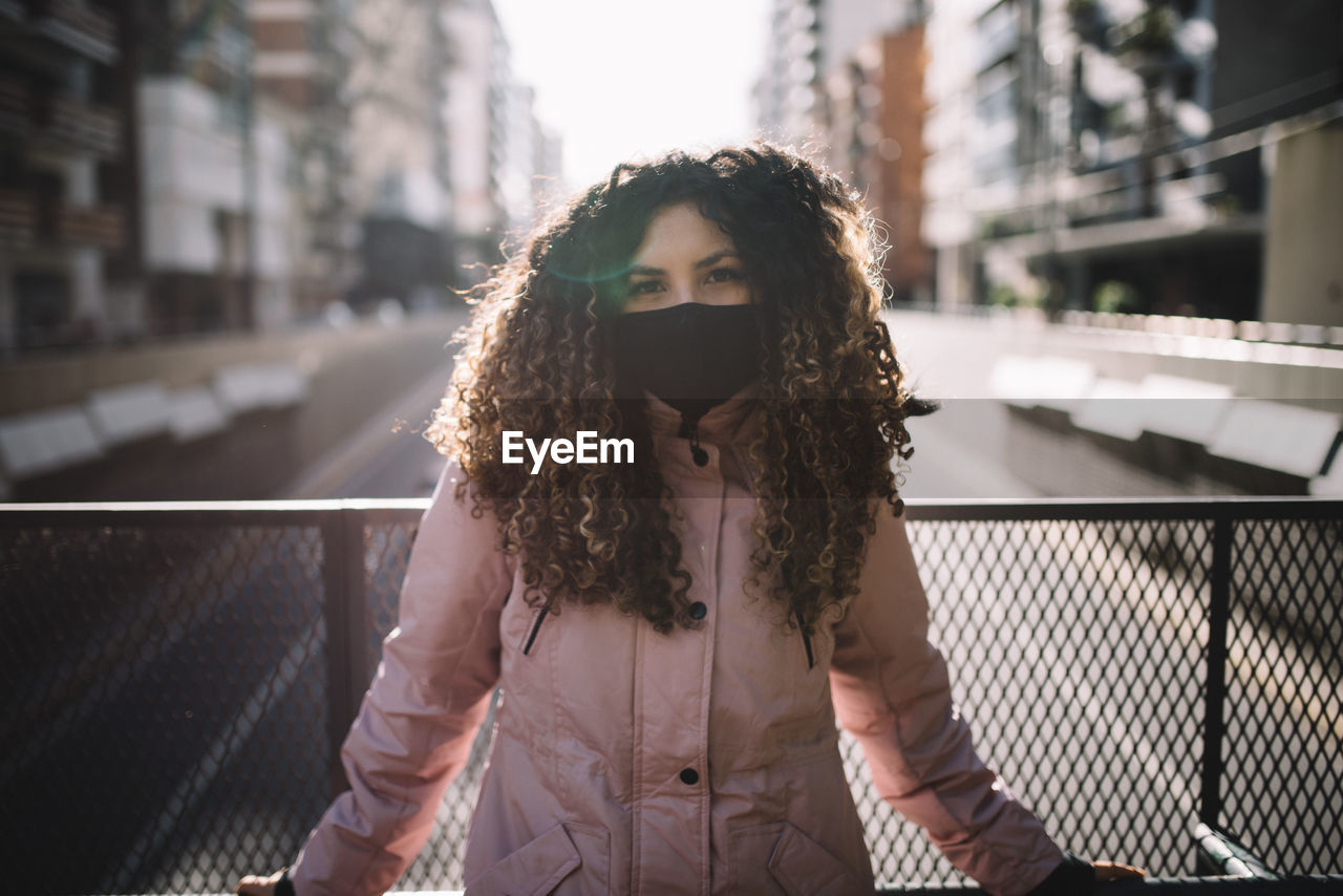 Portrait of young woman standing by railing in city