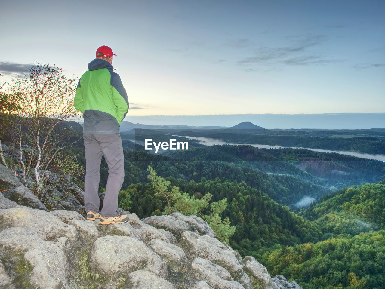 Man stands alone on the peak of rock. hiker watching to autumn sun at horizon . beautiful moment