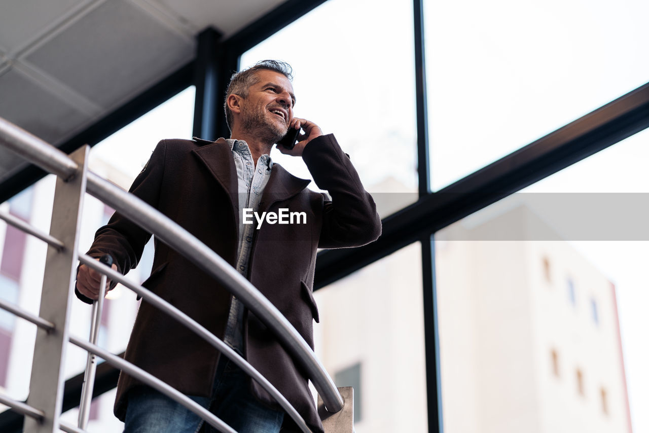 Low angle view of man talking on smart phone near railing