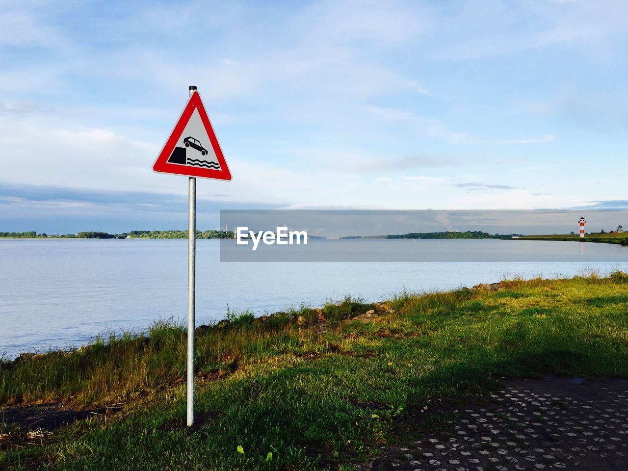 Road sign by river against sky