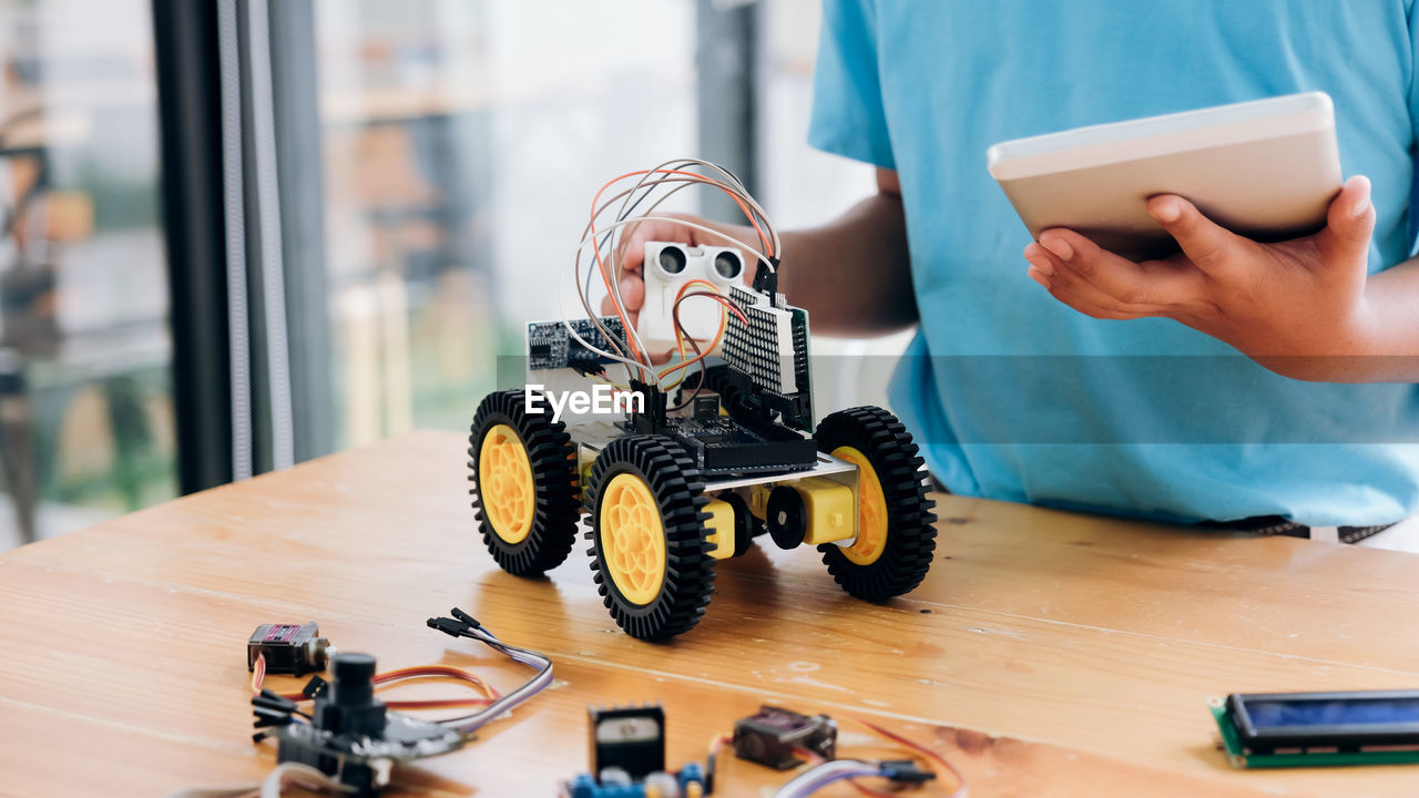 Midsection of boy using digital tablet while repairing toy on table