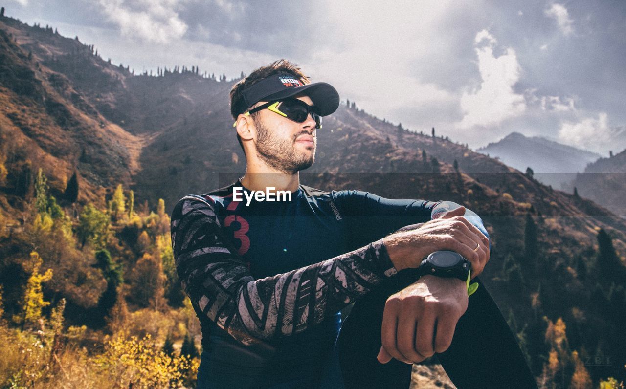 YOUNG MAN WEARING SUNGLASSES STANDING BY MOUNTAIN
