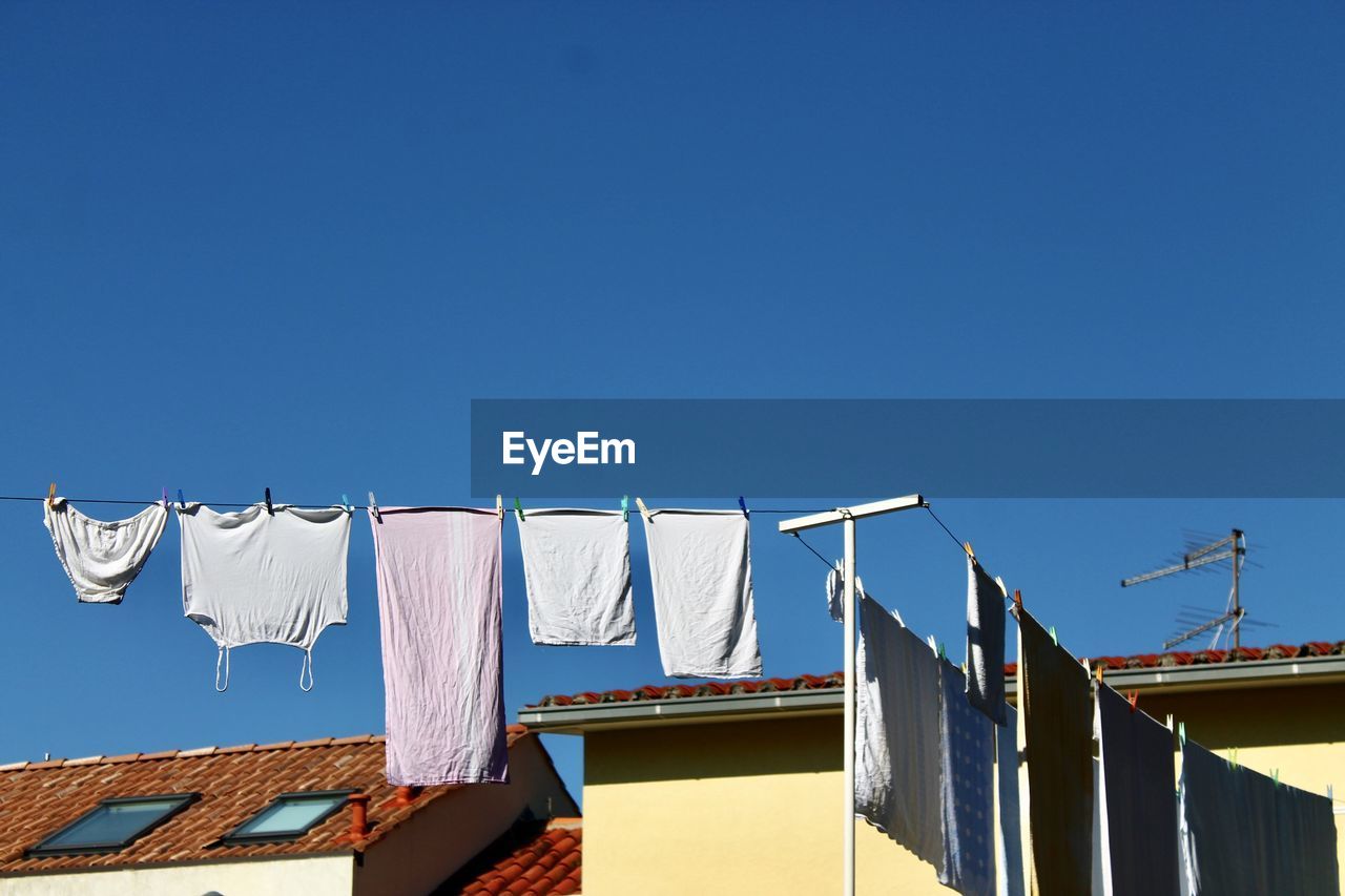 LOW ANGLE VIEW OF CLOTHES DRYING AGAINST BUILDINGS