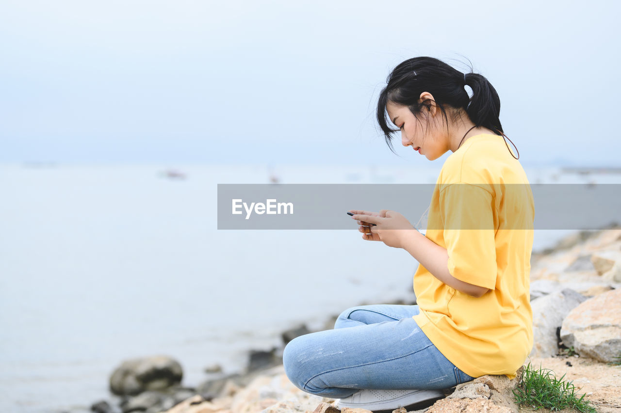 Young man using mobile phone while sitting on beach