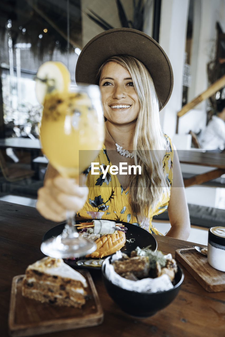 Smiling young woman holding drink at table in restaurant