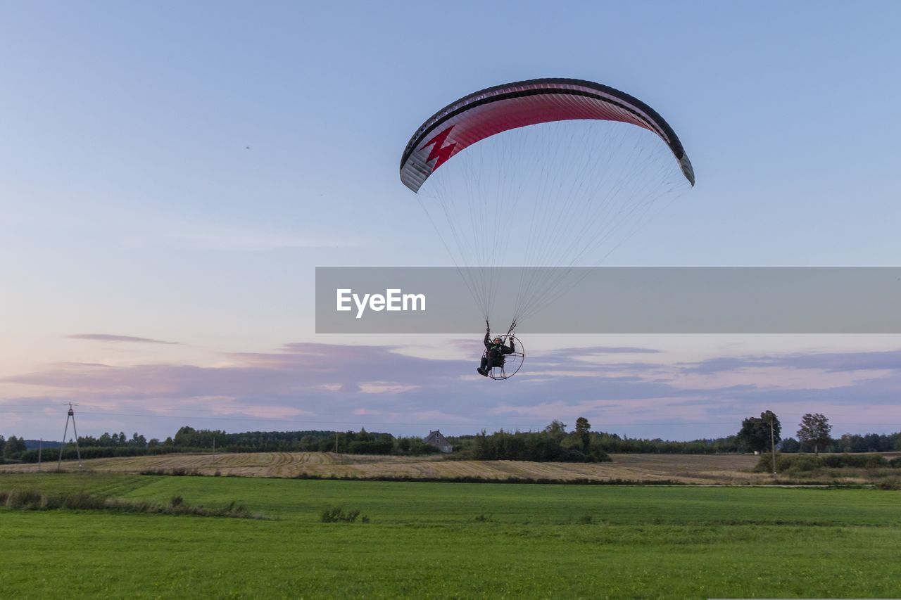 PERSON PARAGLIDING IN FIELD AGAINST SKY