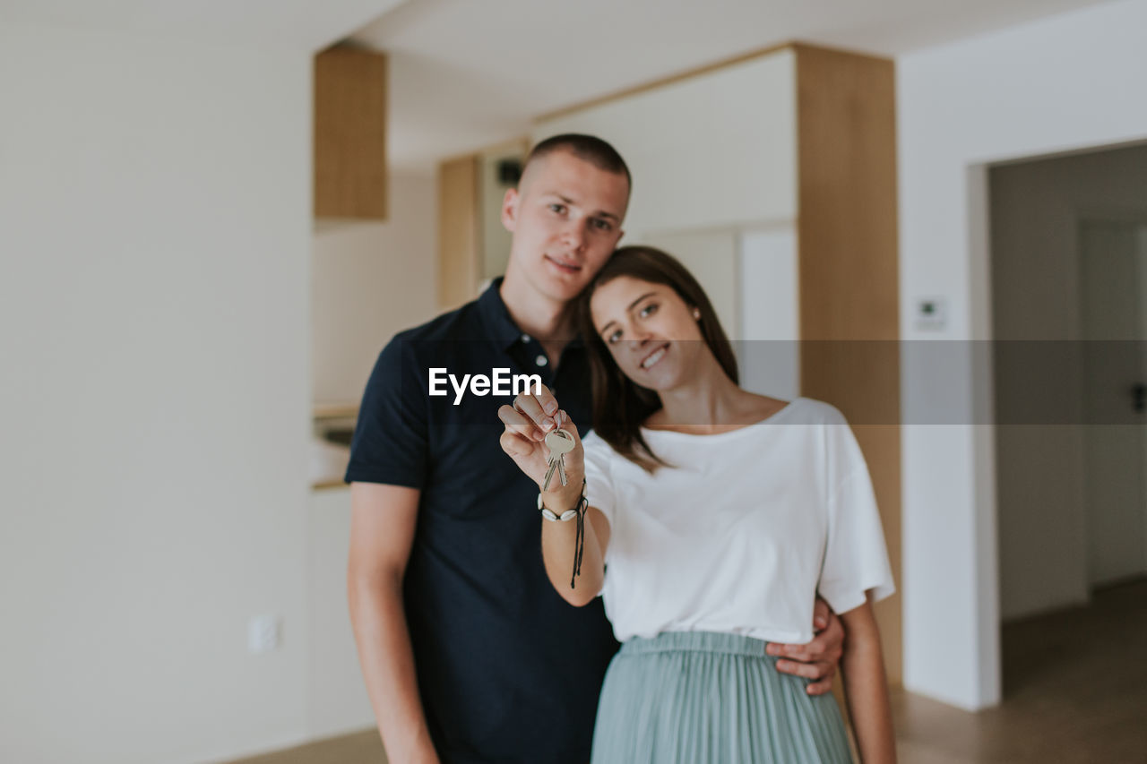 Portrait of smiling young couple with house key standing at home