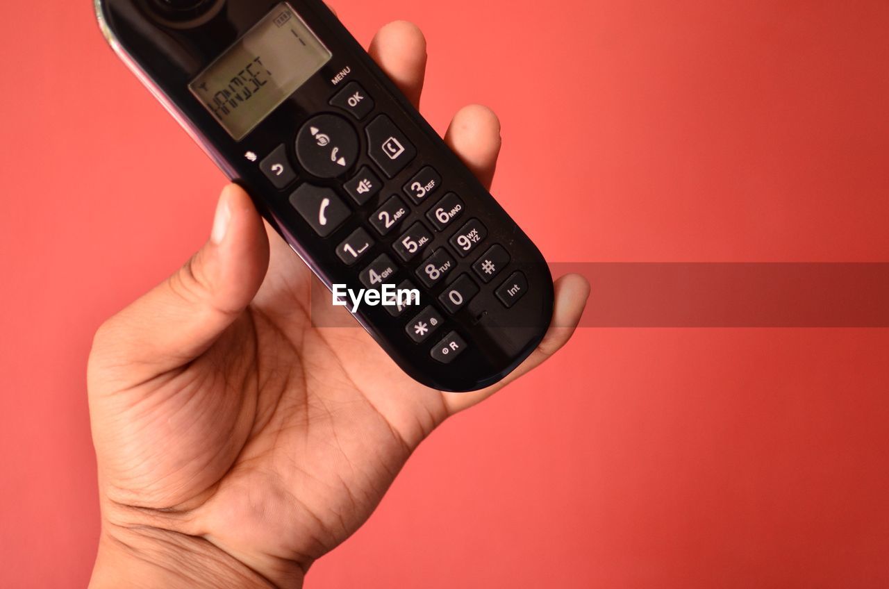 Close-up of cropped hand holding mobile phone against red background