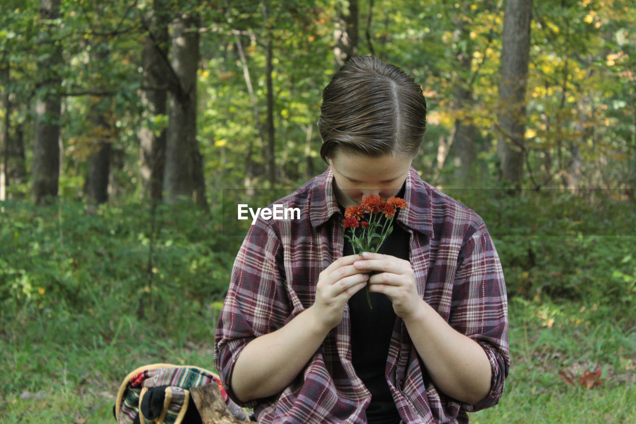 Young man smelling orange flowers while practicing wicca in forest