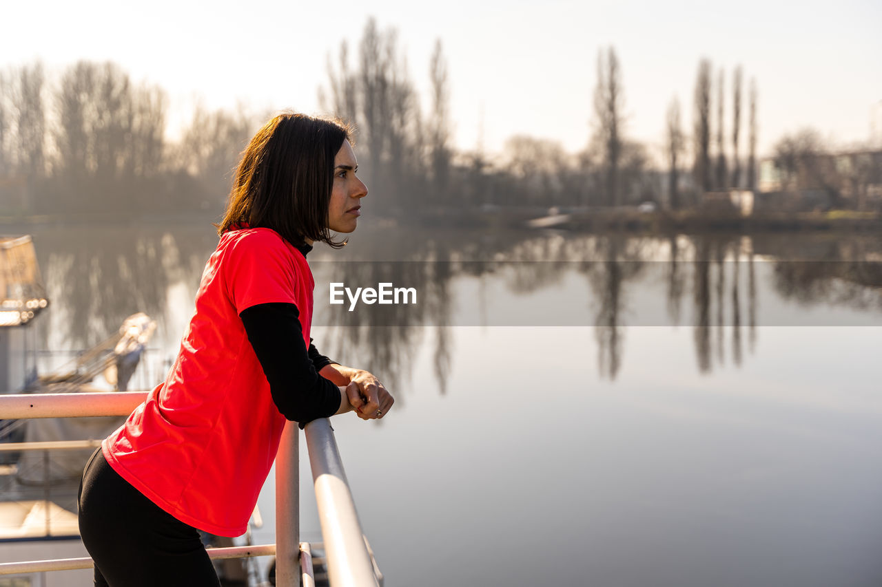 Side view of young woman athlete is taking a break and looks at the river on a boat in the harbor