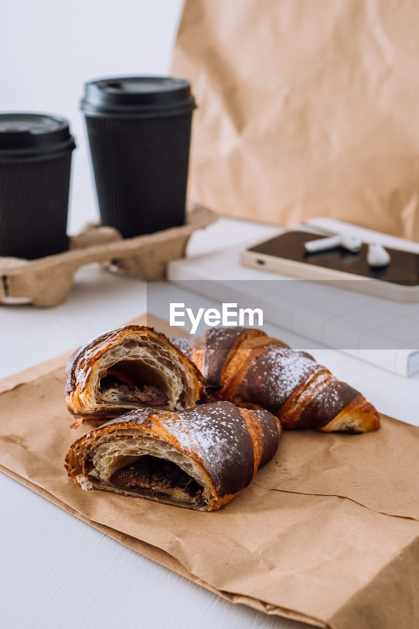 Chocolate croissants with cups of coffee and notepad with smartphone and earphones