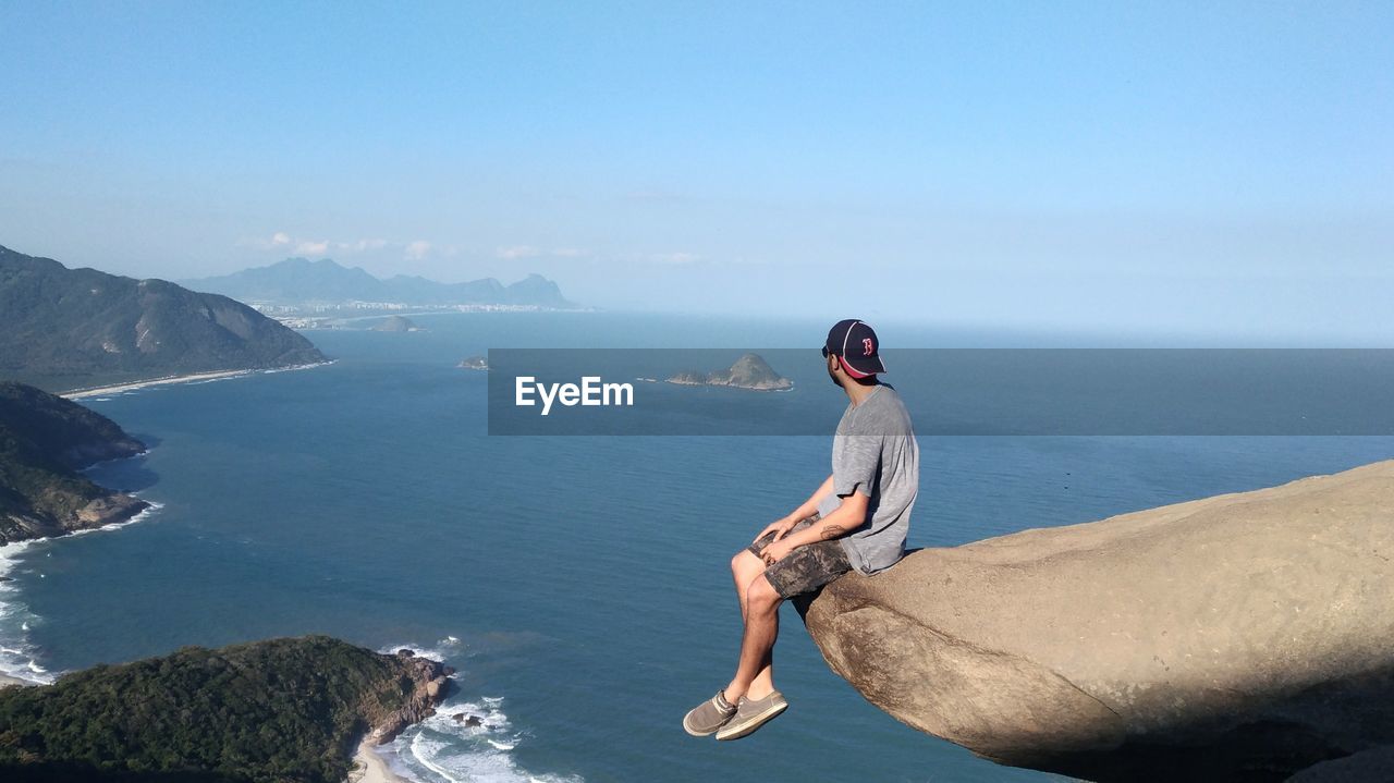 Man sitting on rock over sea against sky