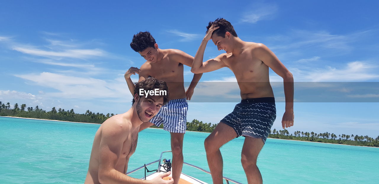 Shirtless friends on boat in sea against sky during sunny day