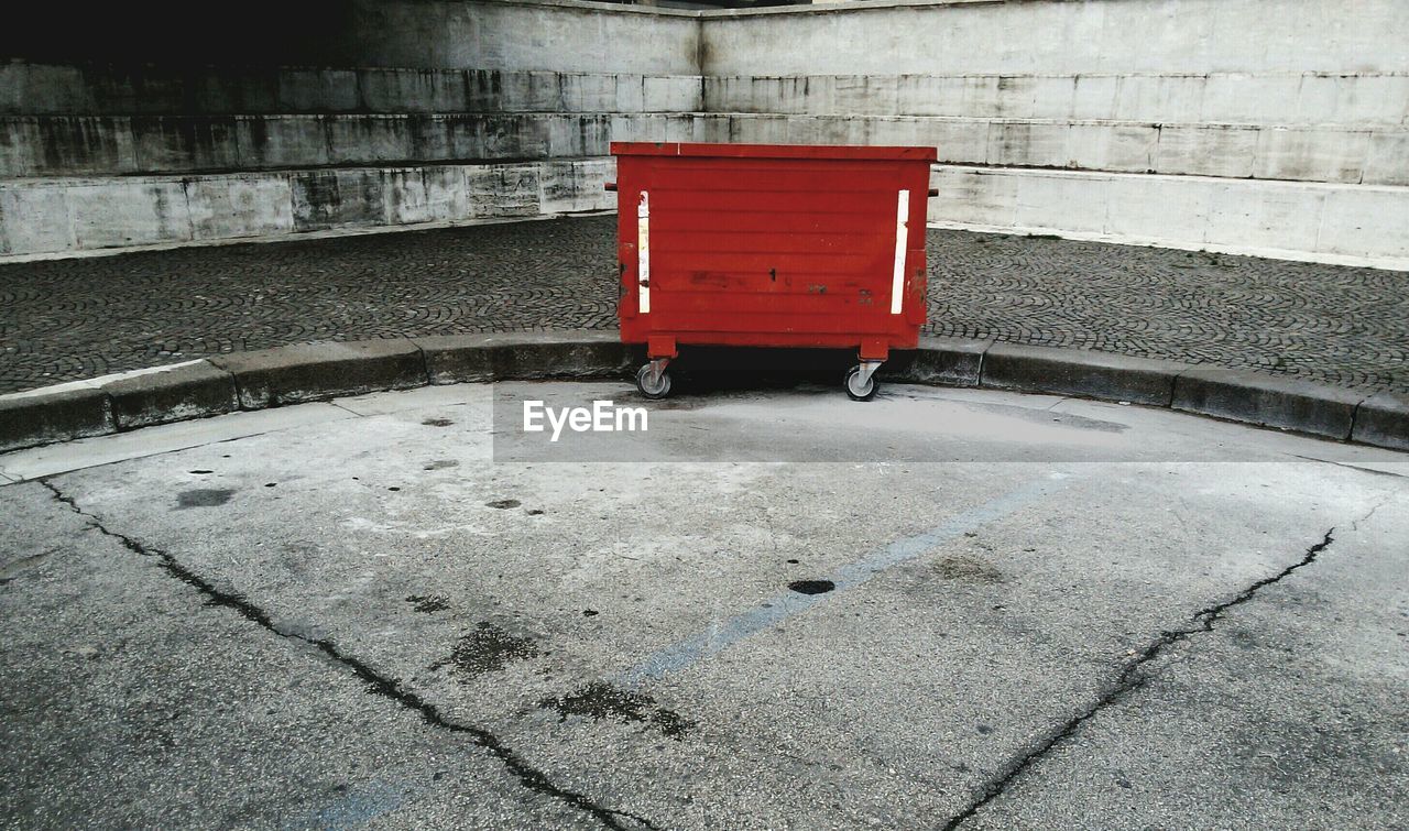 Red garbage bin on footpath against wall