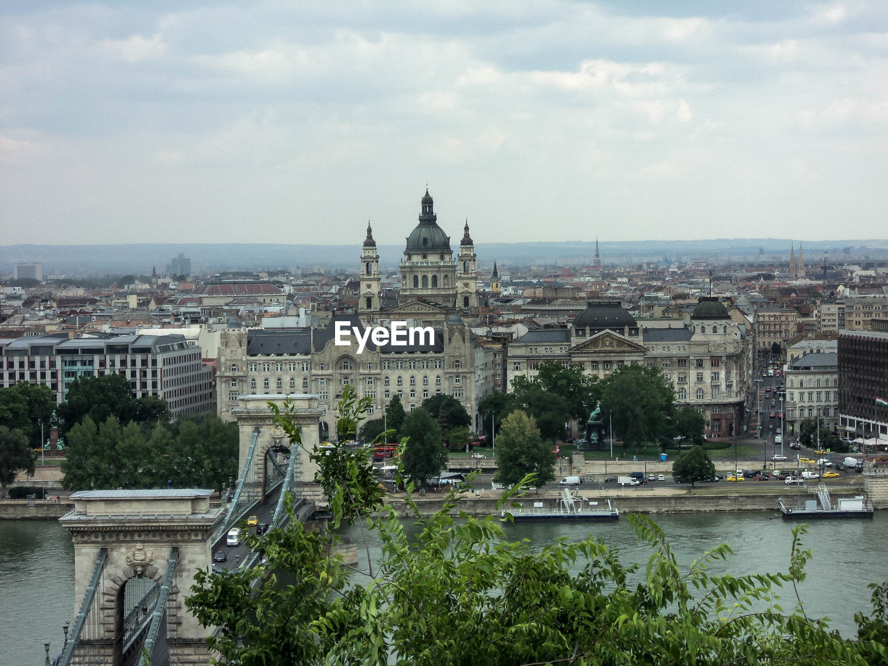 Chain bridge over danube river in city against cloudy sky