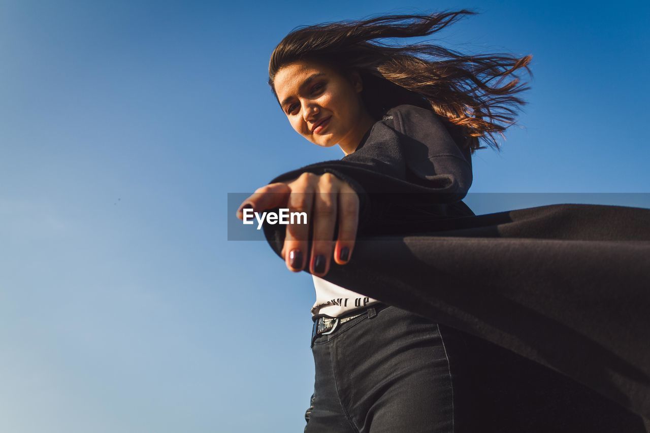 Low angle portrait of woman standing against clear blue sky