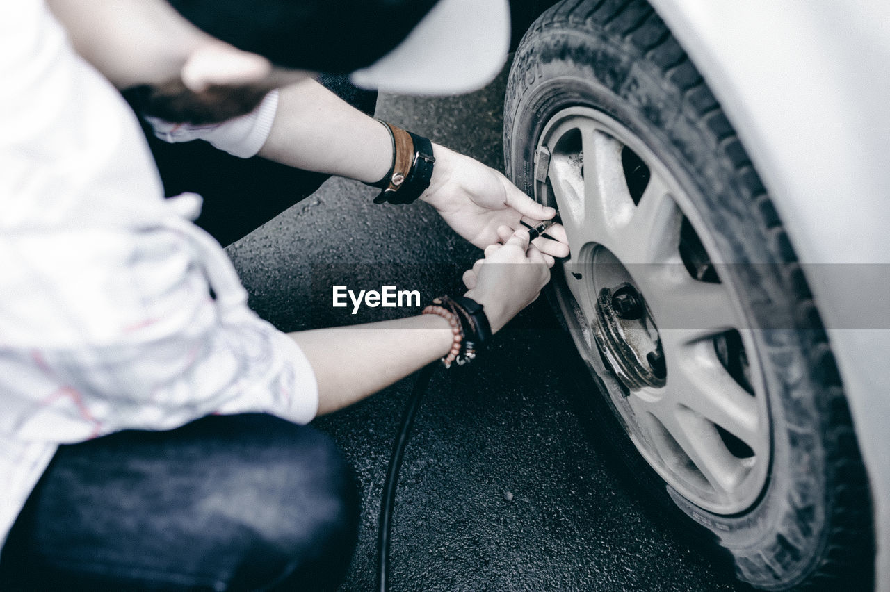 High angle view of man inflating car tire with air pump at parking lot