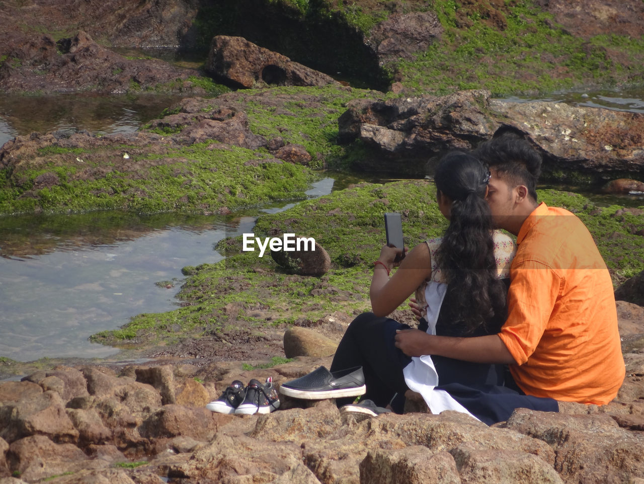 Rear view of couple photographing while sitting on rock 