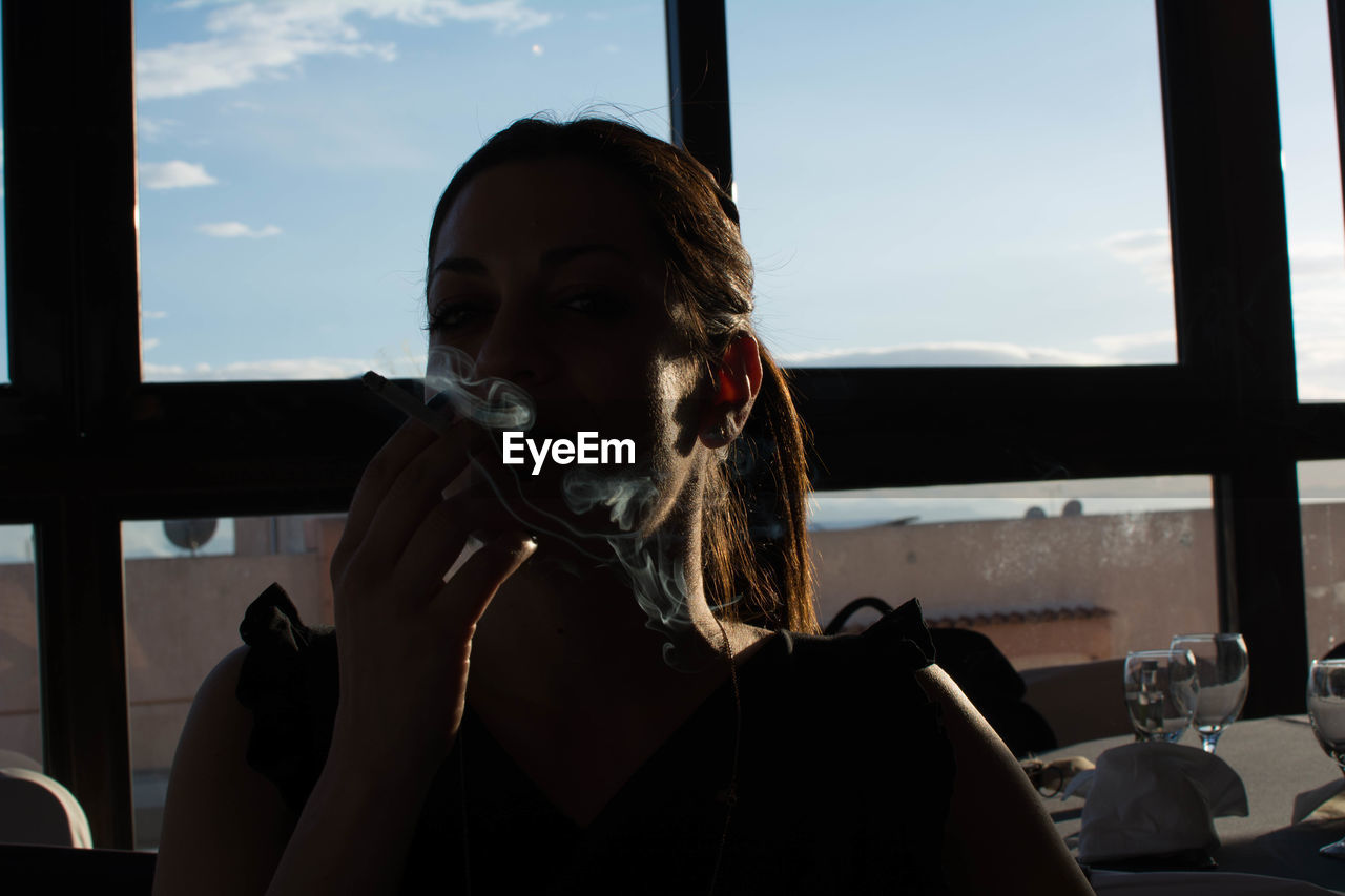 Woman smoking cigarette in restaurant against window