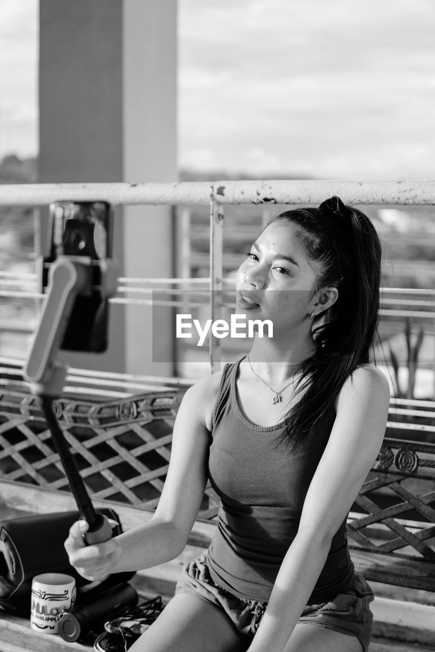 Portrait of young woman looking away while sitting on railing