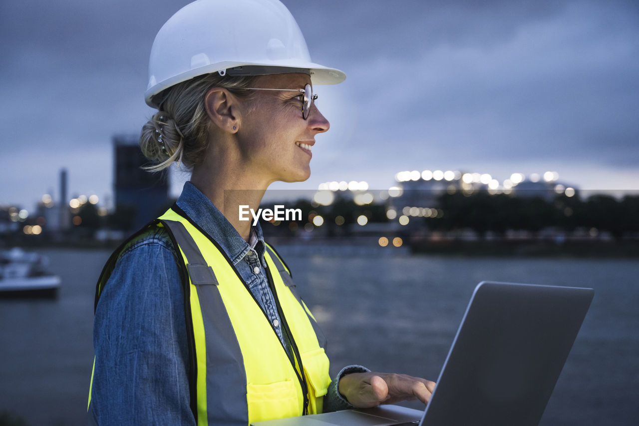 Thoughtful female professional smiling while holding laptop