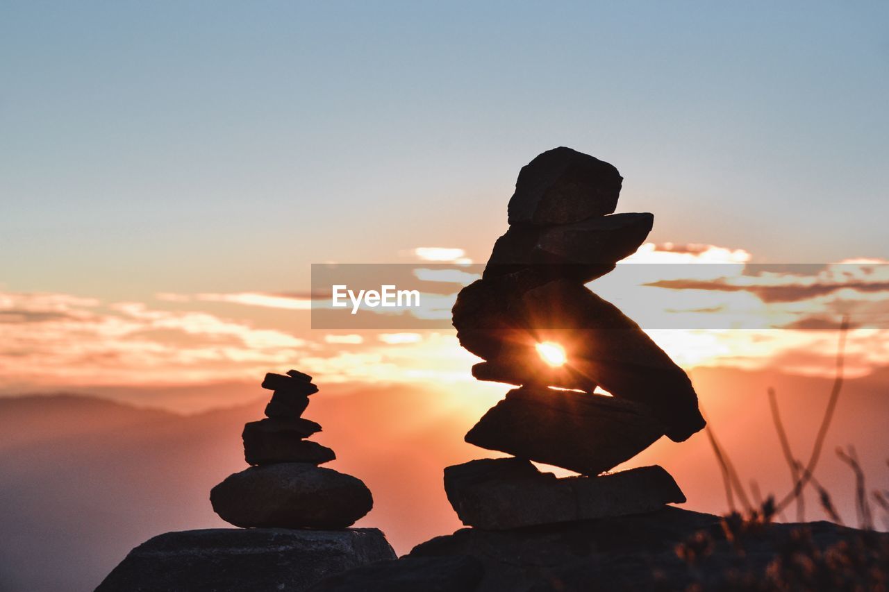 Close-up of silhouette stacked pebbles rocks on field against orange sky