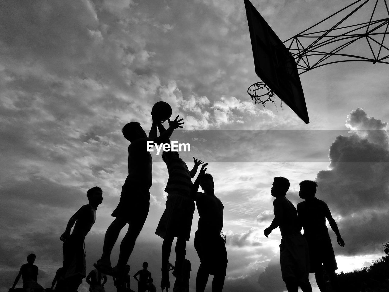 Low angle view of silhouette friends playing basketball against cloudy sky