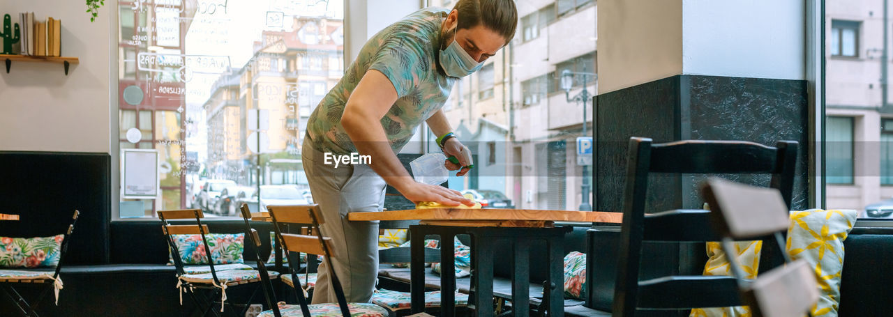 Man wearing mask cleaning table in cafe