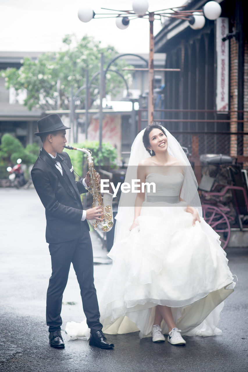 Full length of man playing saxophone while bride walking on road