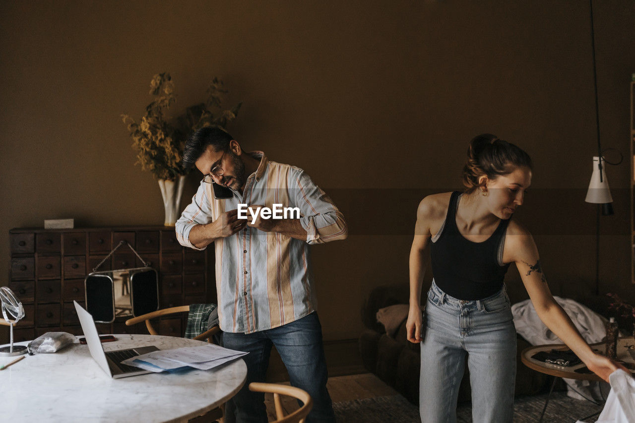 Man buttoning shirt while standing with non-binary person at home