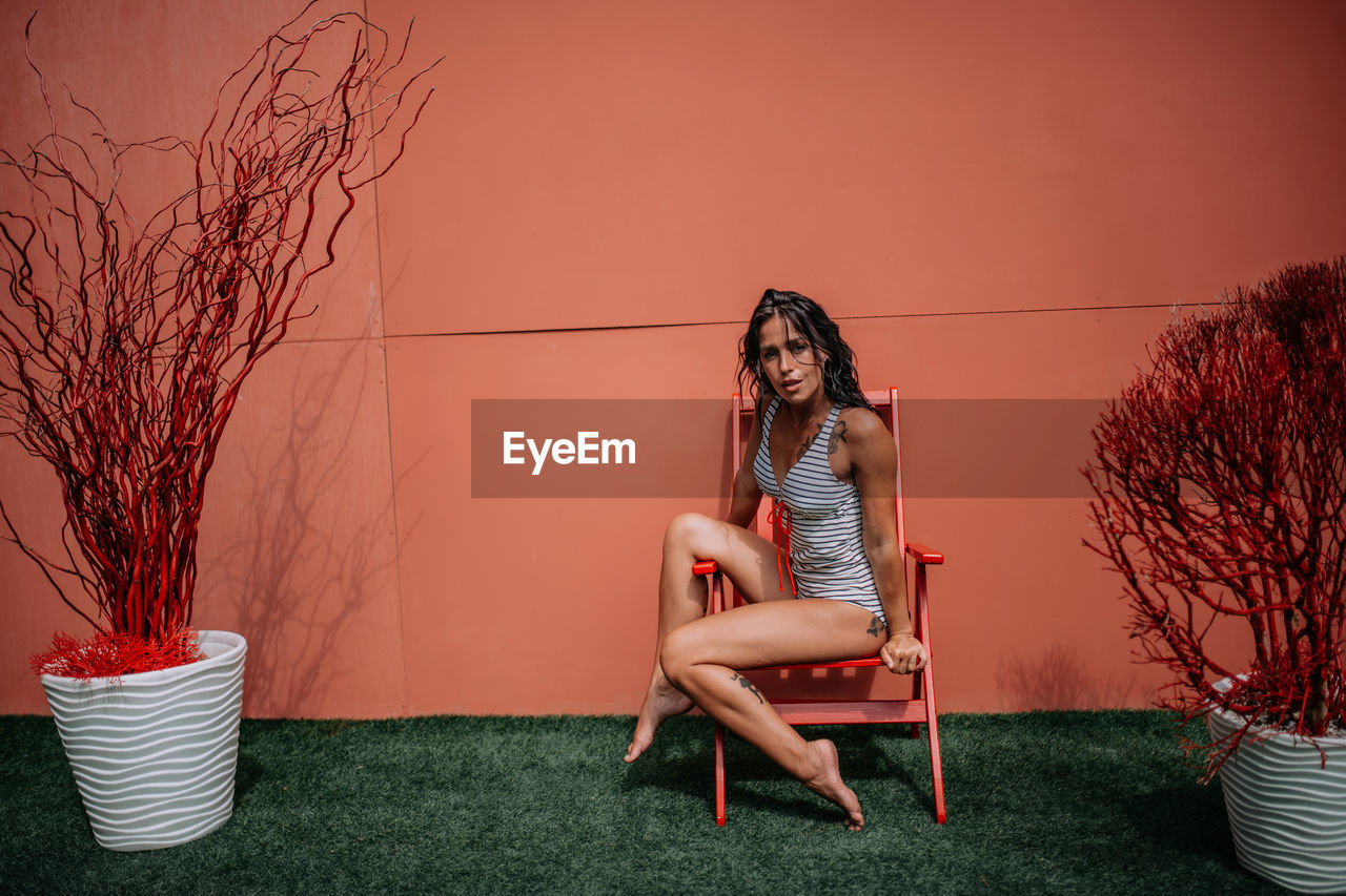 Woman sitting on chair against plants against wall