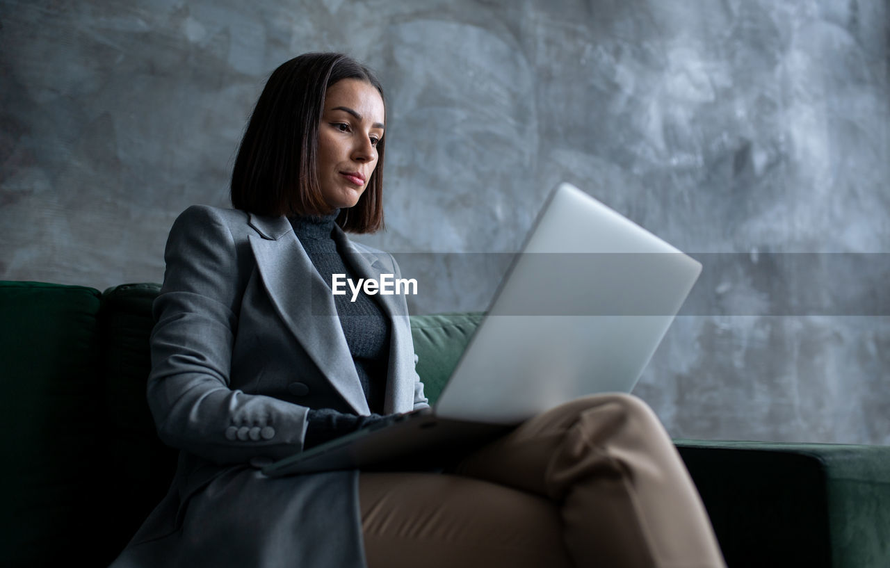 Young female manager sitting on green sofa in loft living room.