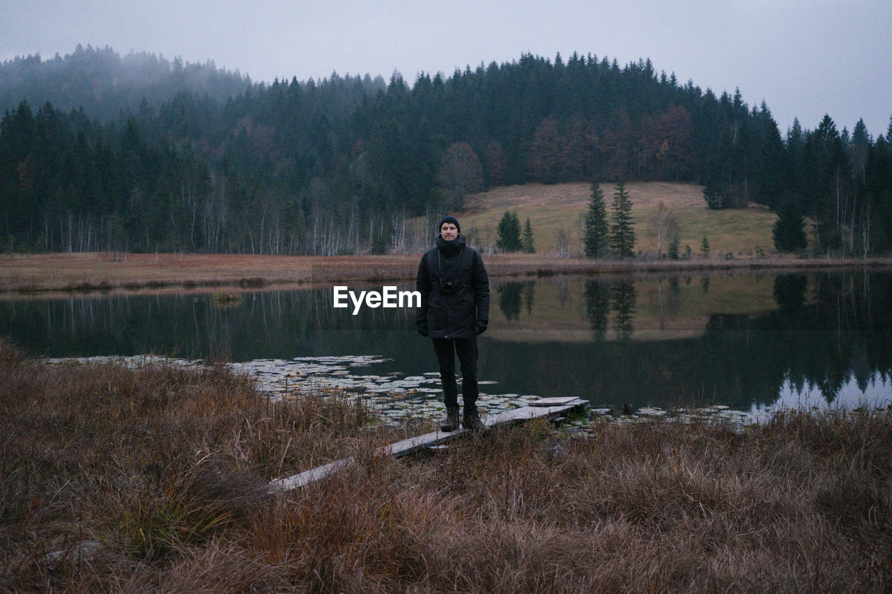 Man standing against lake and trees