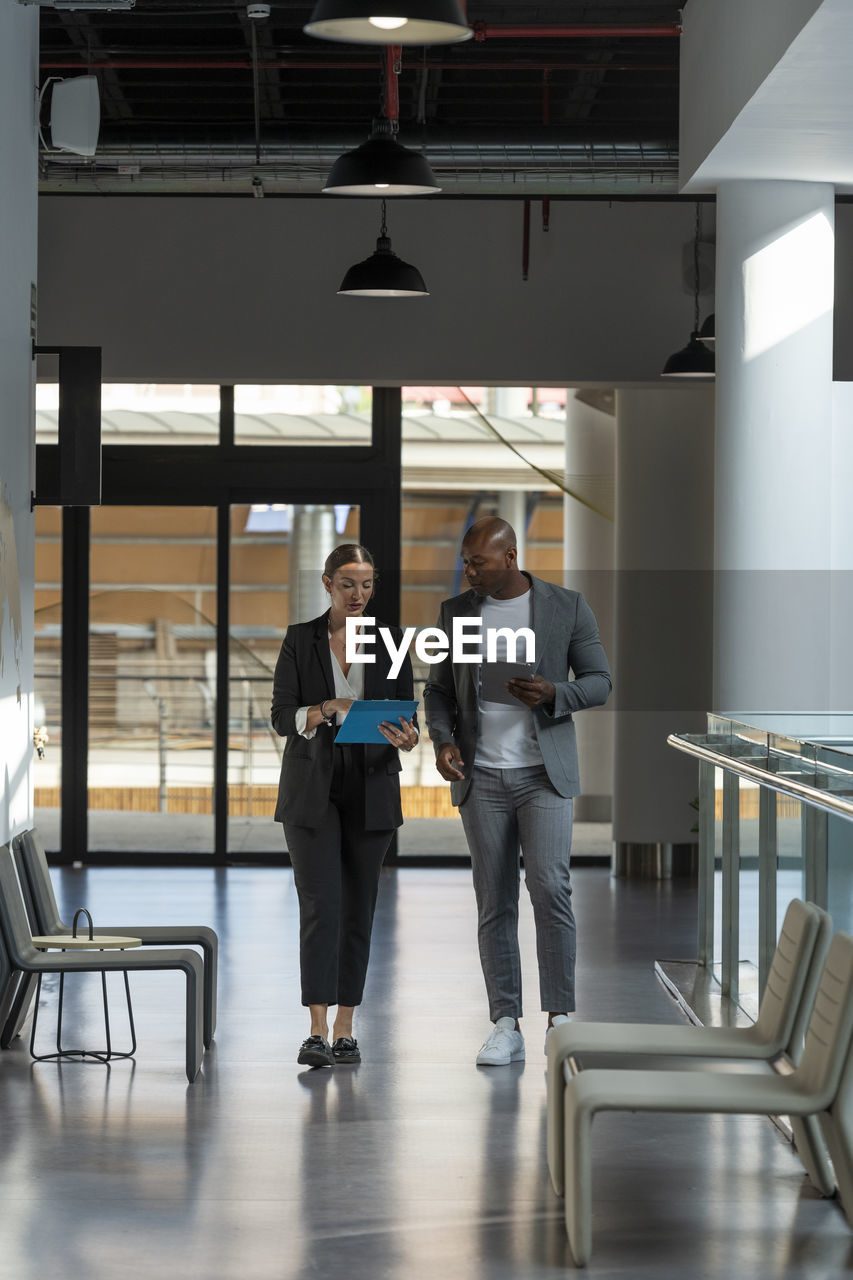 Business colleagues walking and discussing over clipboard in office corridor