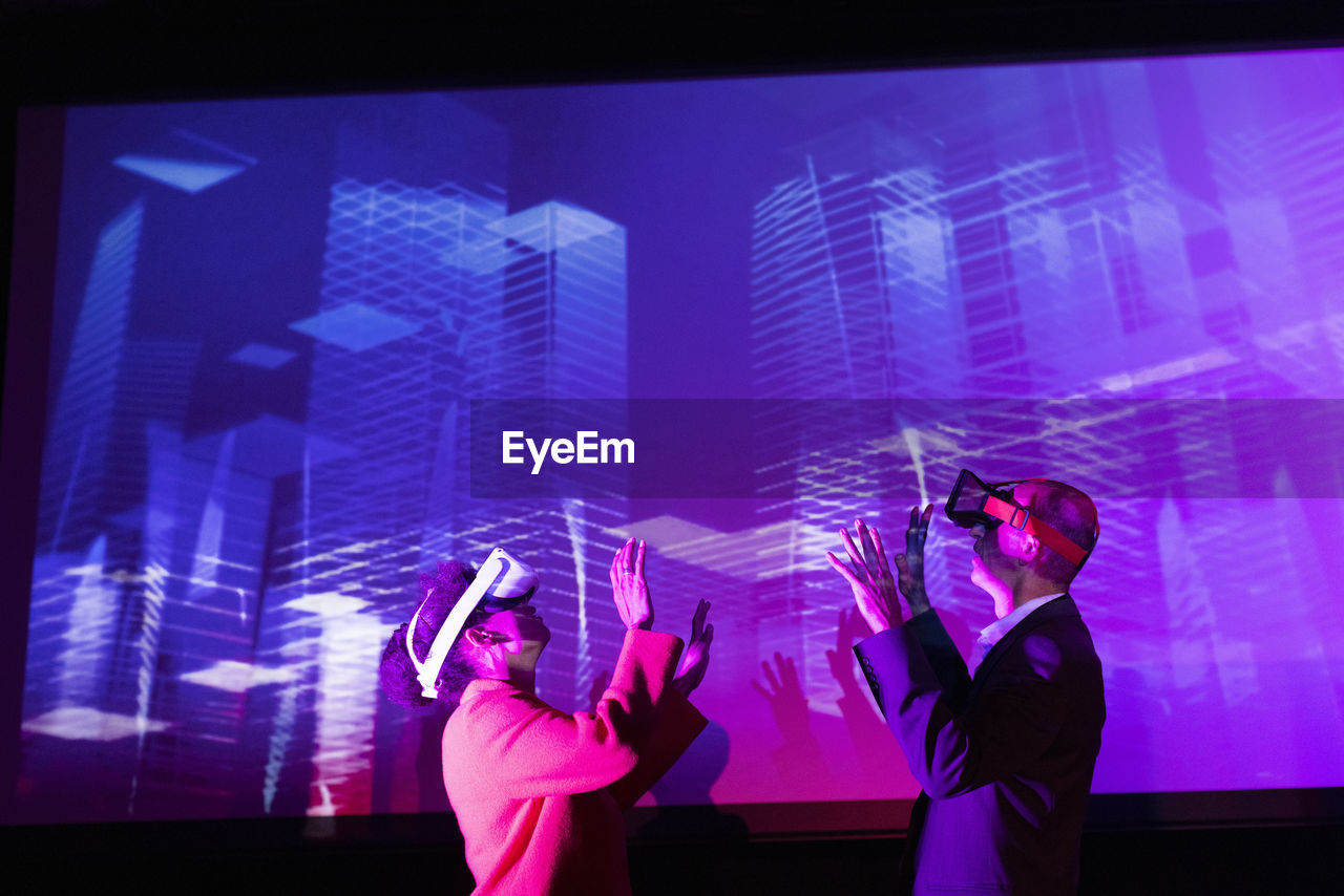 Business colleagues with futuristic glasses gesturing by projection screen at convention center