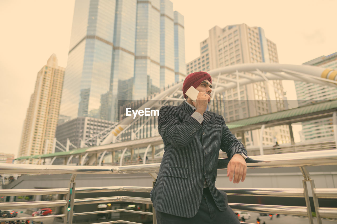 FULL LENGTH OF MAN STANDING ON RAILING AGAINST BUILDINGS