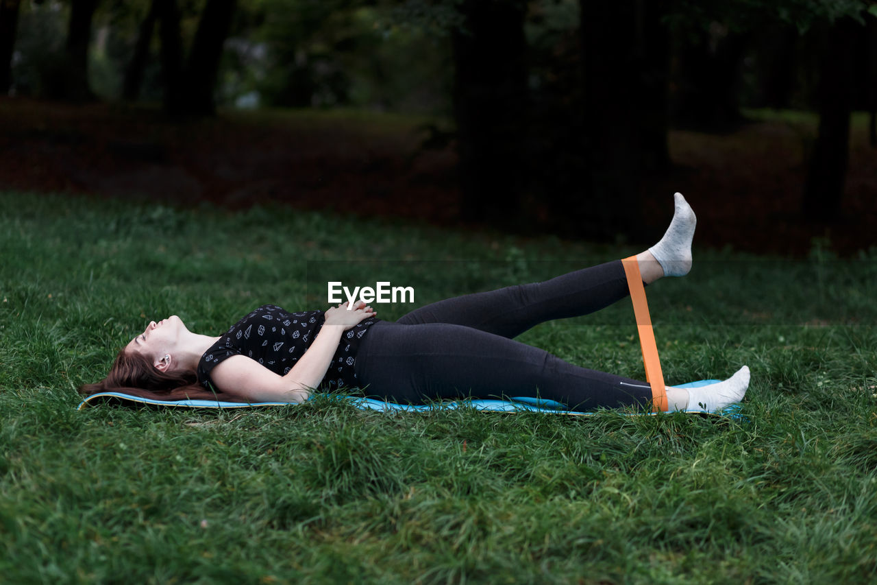 Girl is stretching with a rubber band on a yoga mat in the park