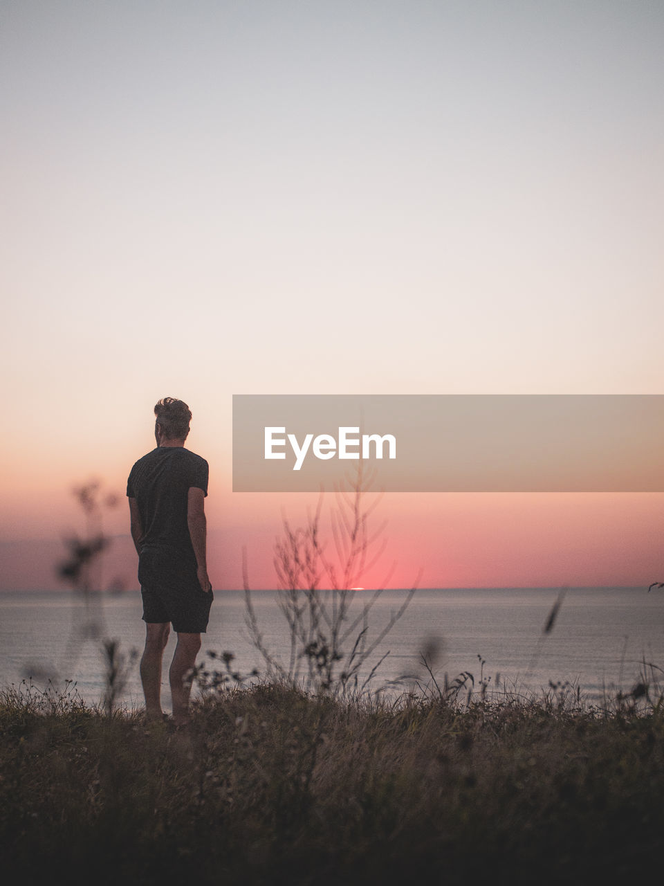 Rear view of man standing on beach during sunset