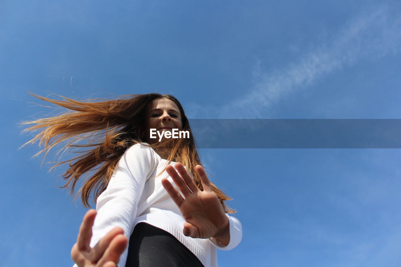 Low angle portrait of woman standing against blue sky