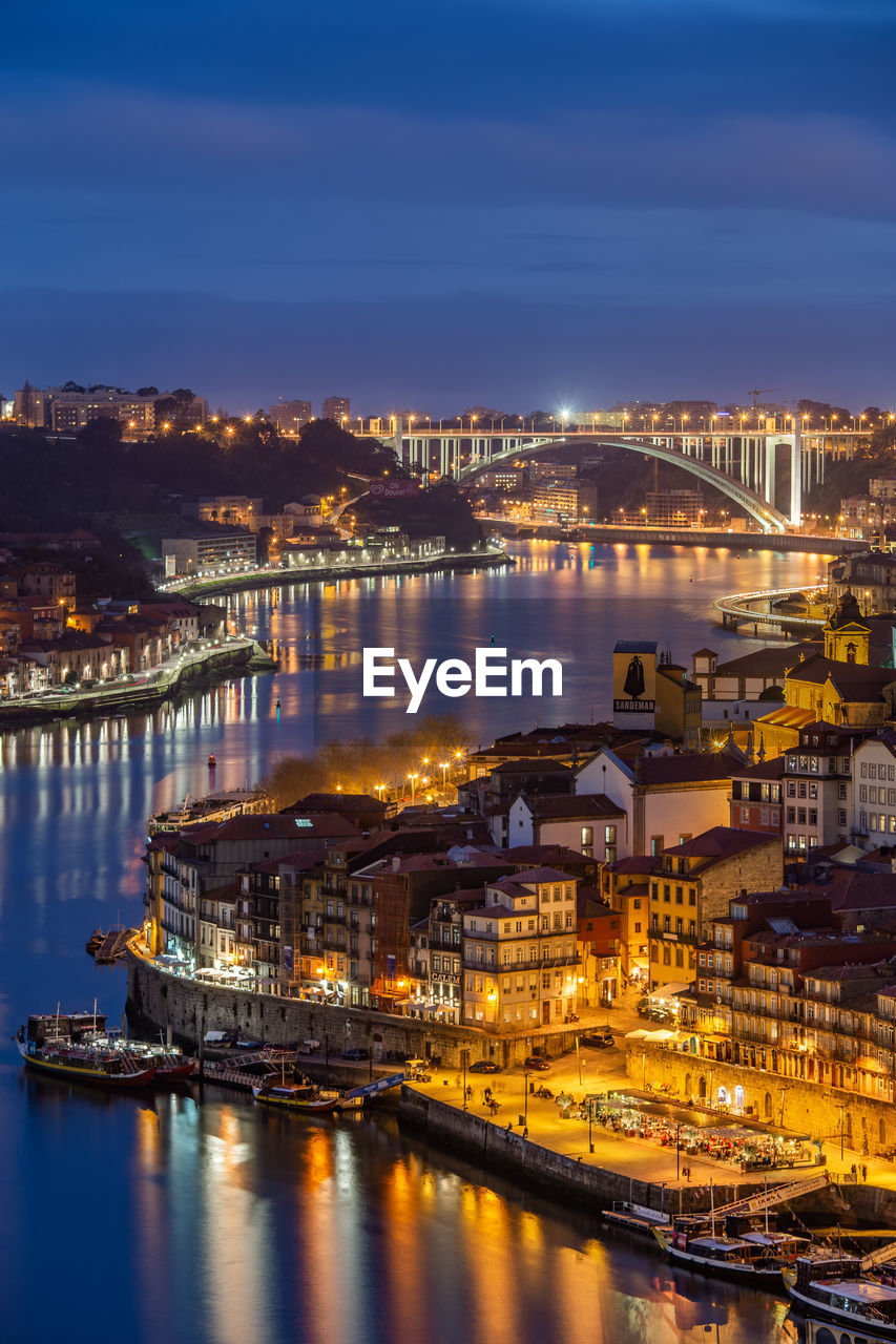 ILLUMINATED BUILDINGS BY RIVER AGAINST SKY AT NIGHT IN CITY