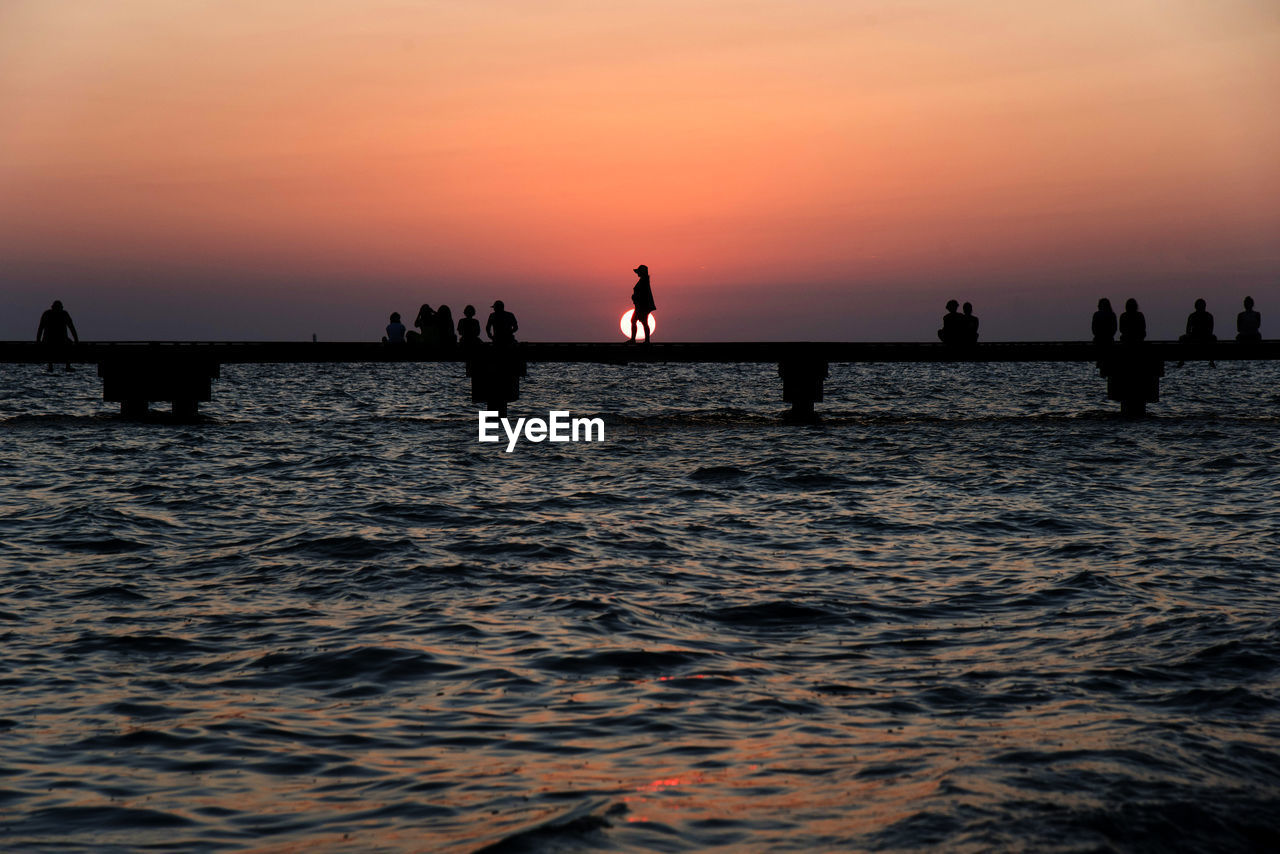 Silhouette of people over sea during sunset