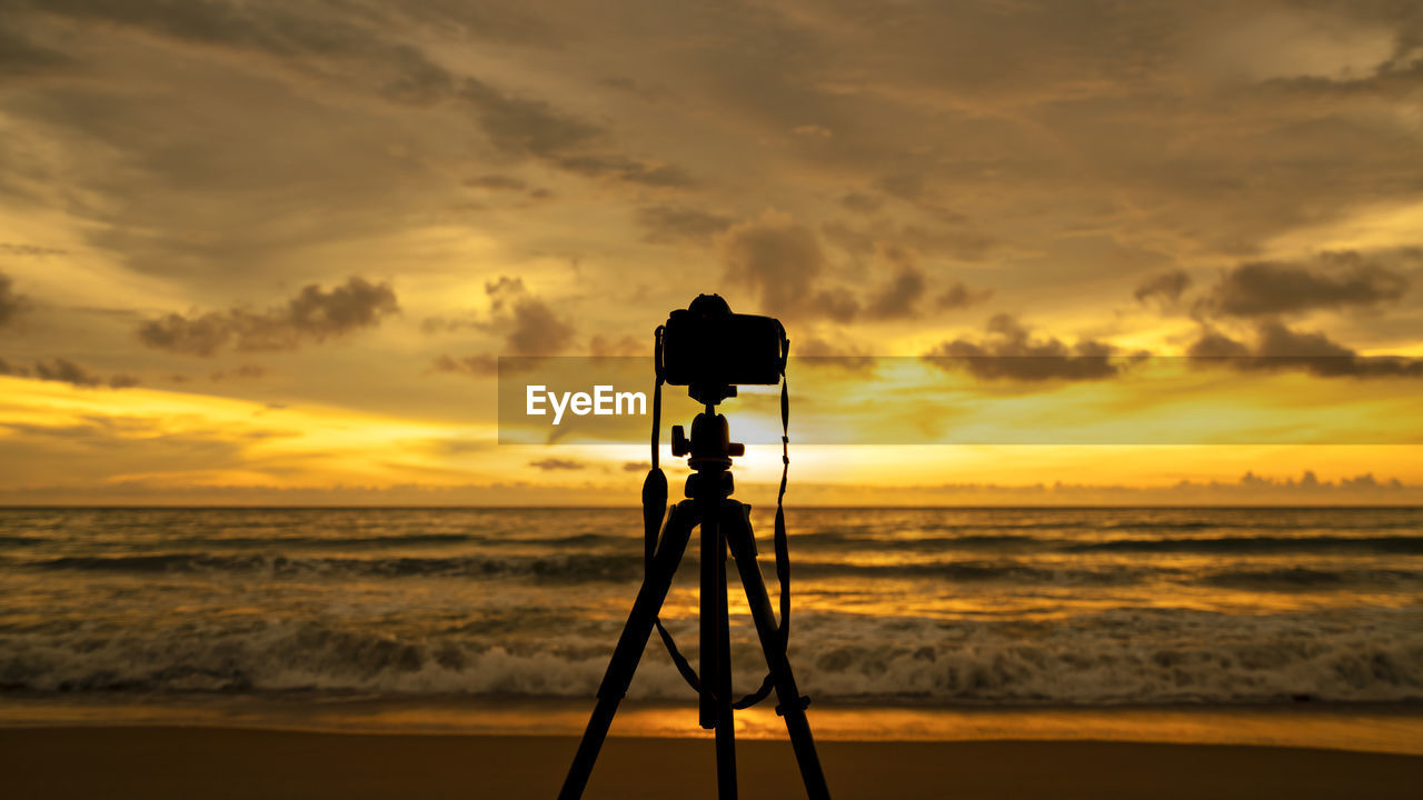 Silhouette camera on beach against sky during sunset